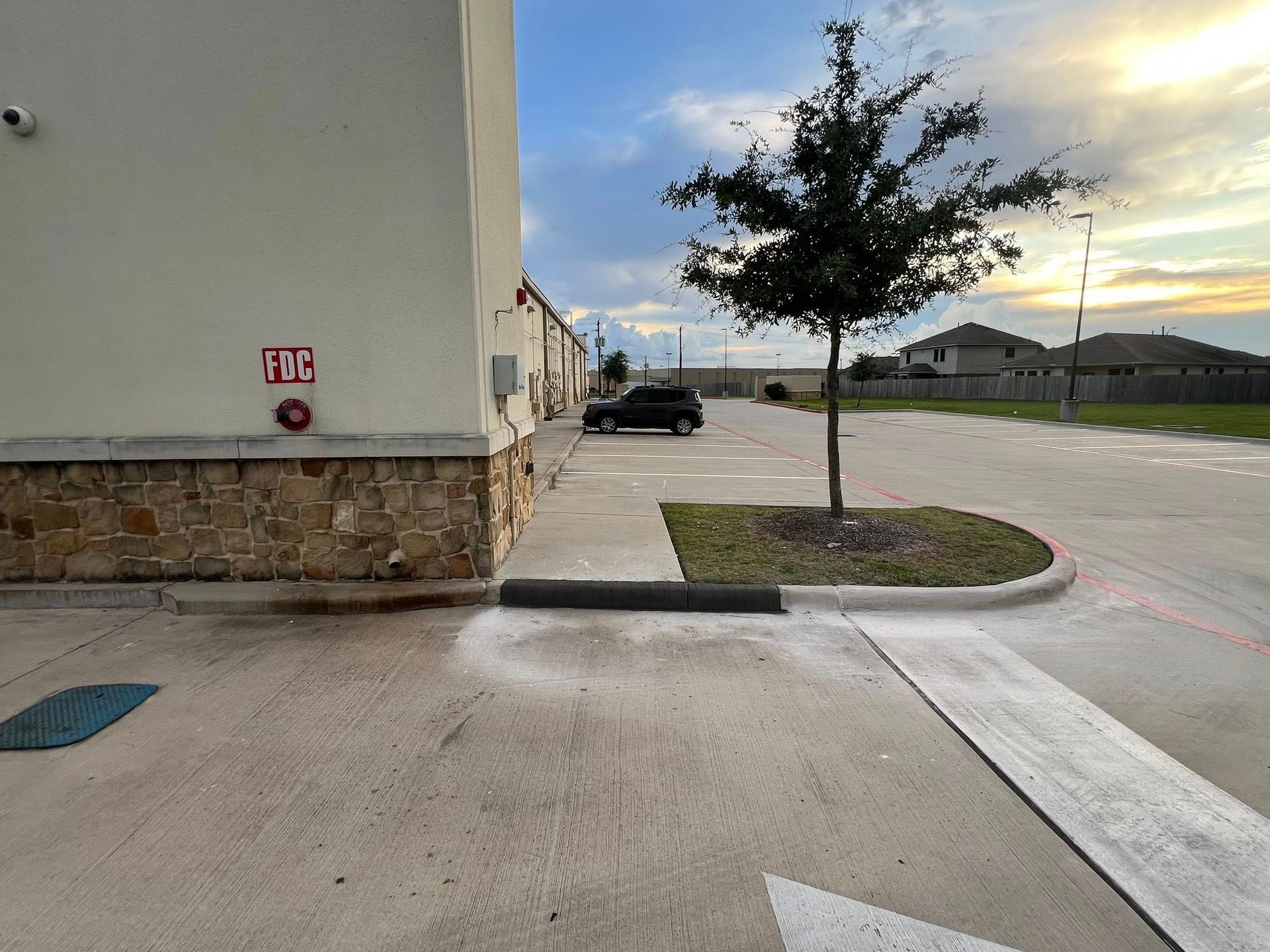 Exterior of a building with a parking lot. A car is parked, a tree, and cloudy sky.