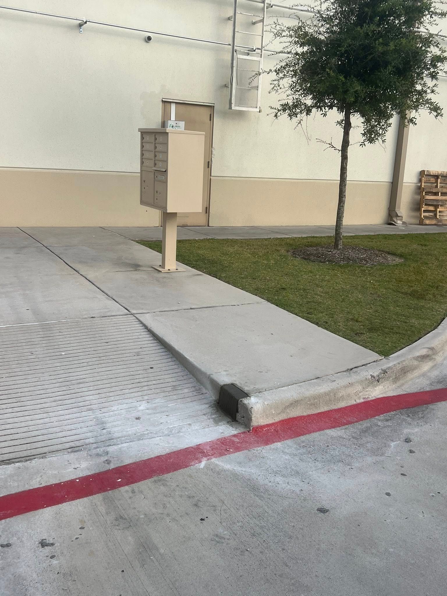 Mailboxes on a concrete path next to a building and grass. Red stripe runs along the path.