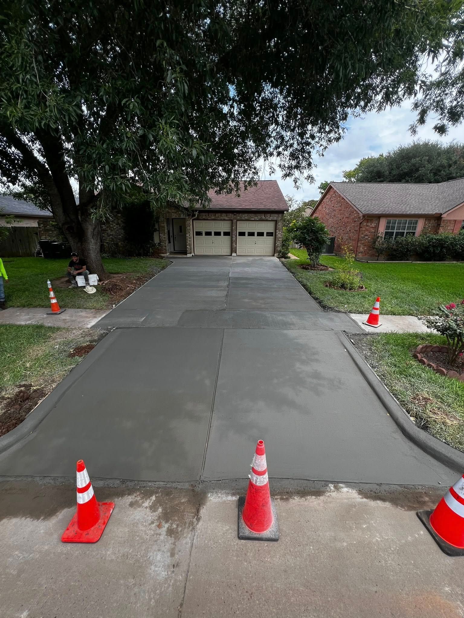 Newly poured concrete driveway with safety cones, leading to a two-car garage under a cloudy sky.