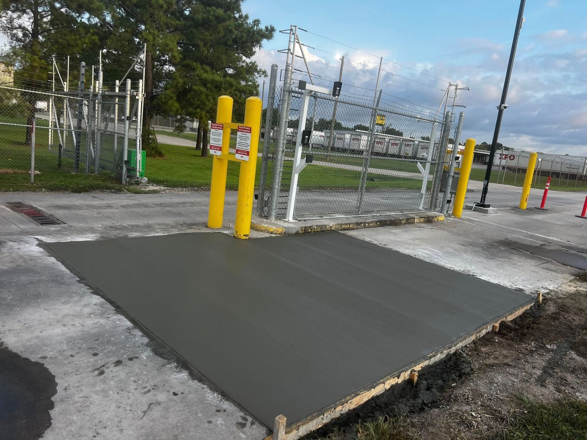 Fresh concrete pad in front of a gated industrial area. Yellow posts frame the gate.