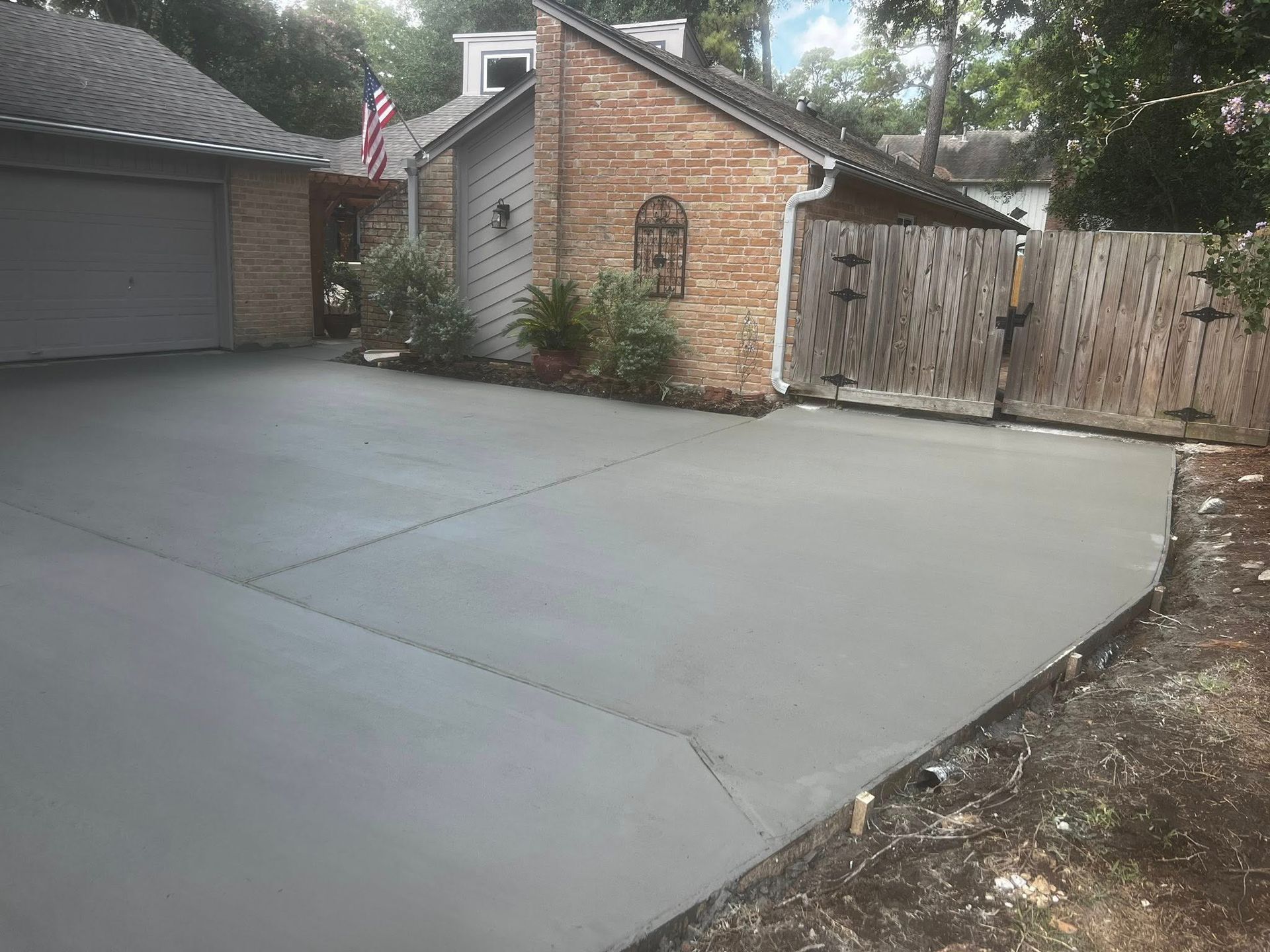 Newly poured concrete driveway in front of a brick house with a garage and wooden fence.