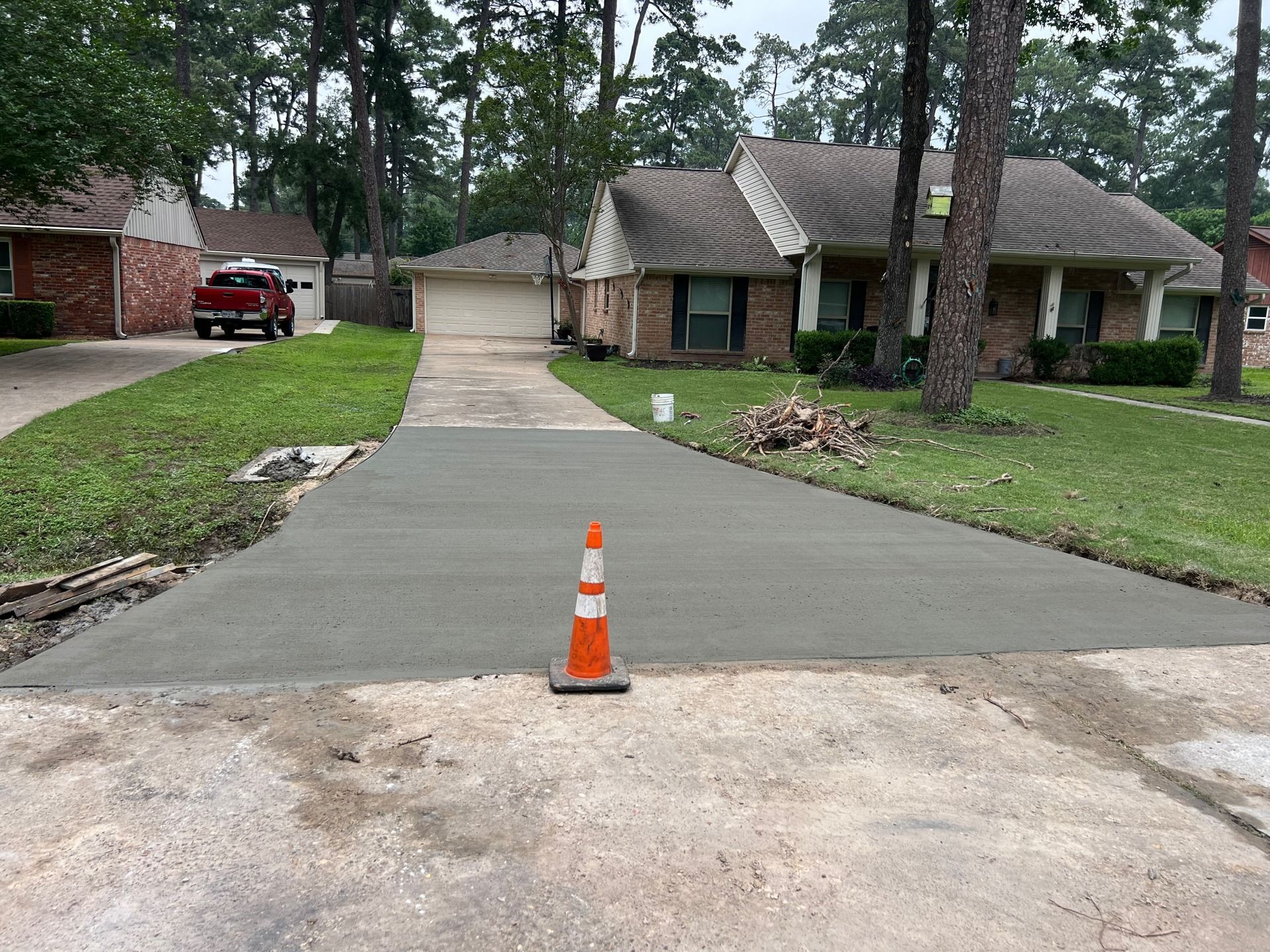 Freshly poured concrete driveway with an orange cone, suburban home in the background.