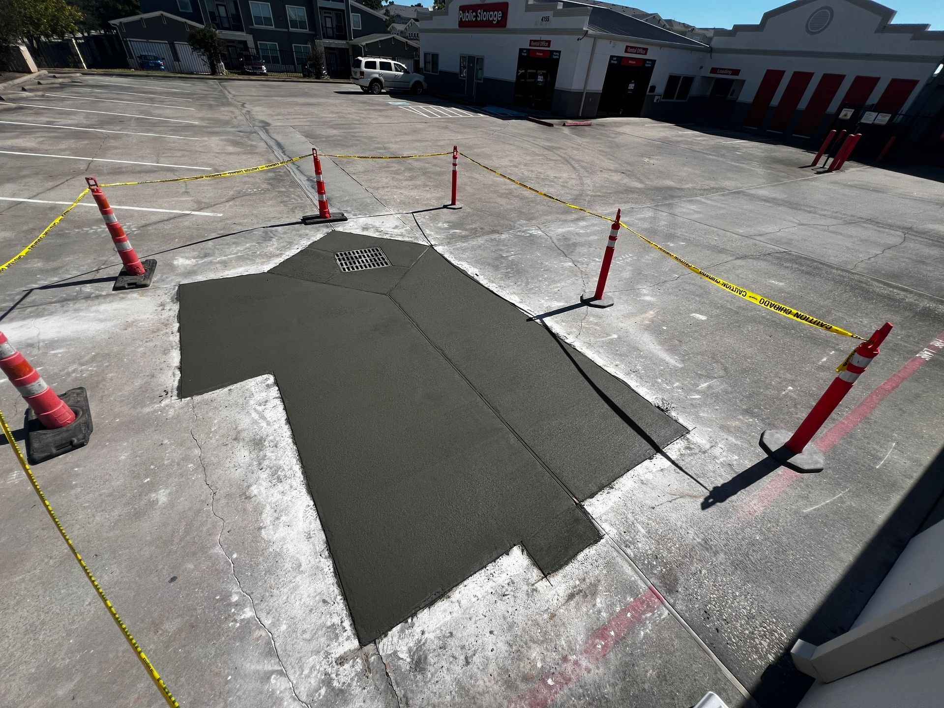 A newly paved asphalt patch in a parking lot, surrounded by caution tape and cones.