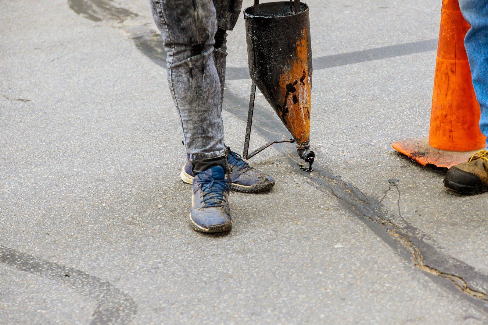 Person repairing asphalt crack with a hot-pour sealant and a dispensing tool.