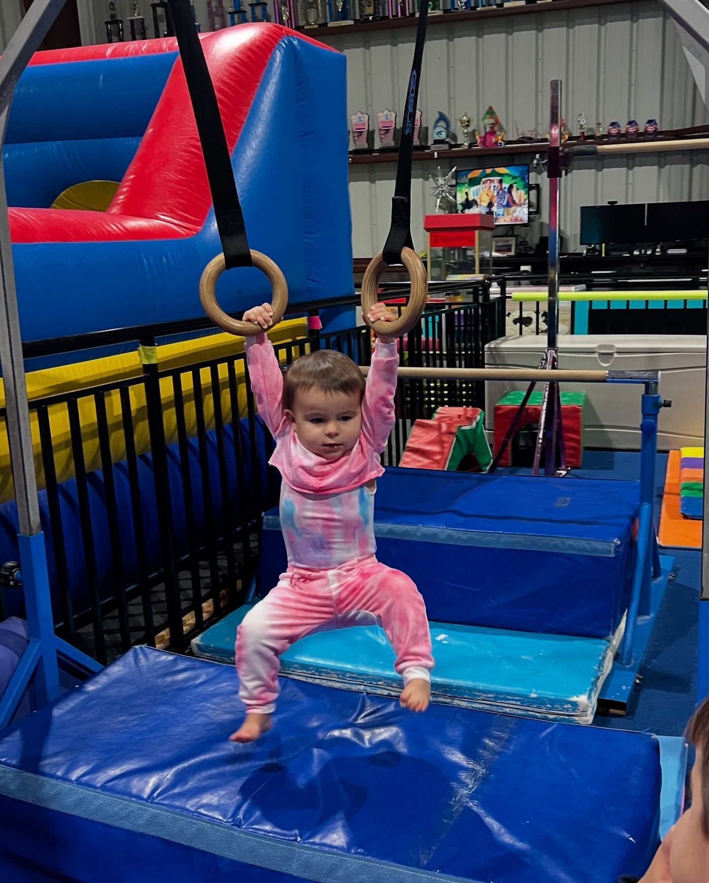 A little girl is playing on gymnastic rings in a gym.
