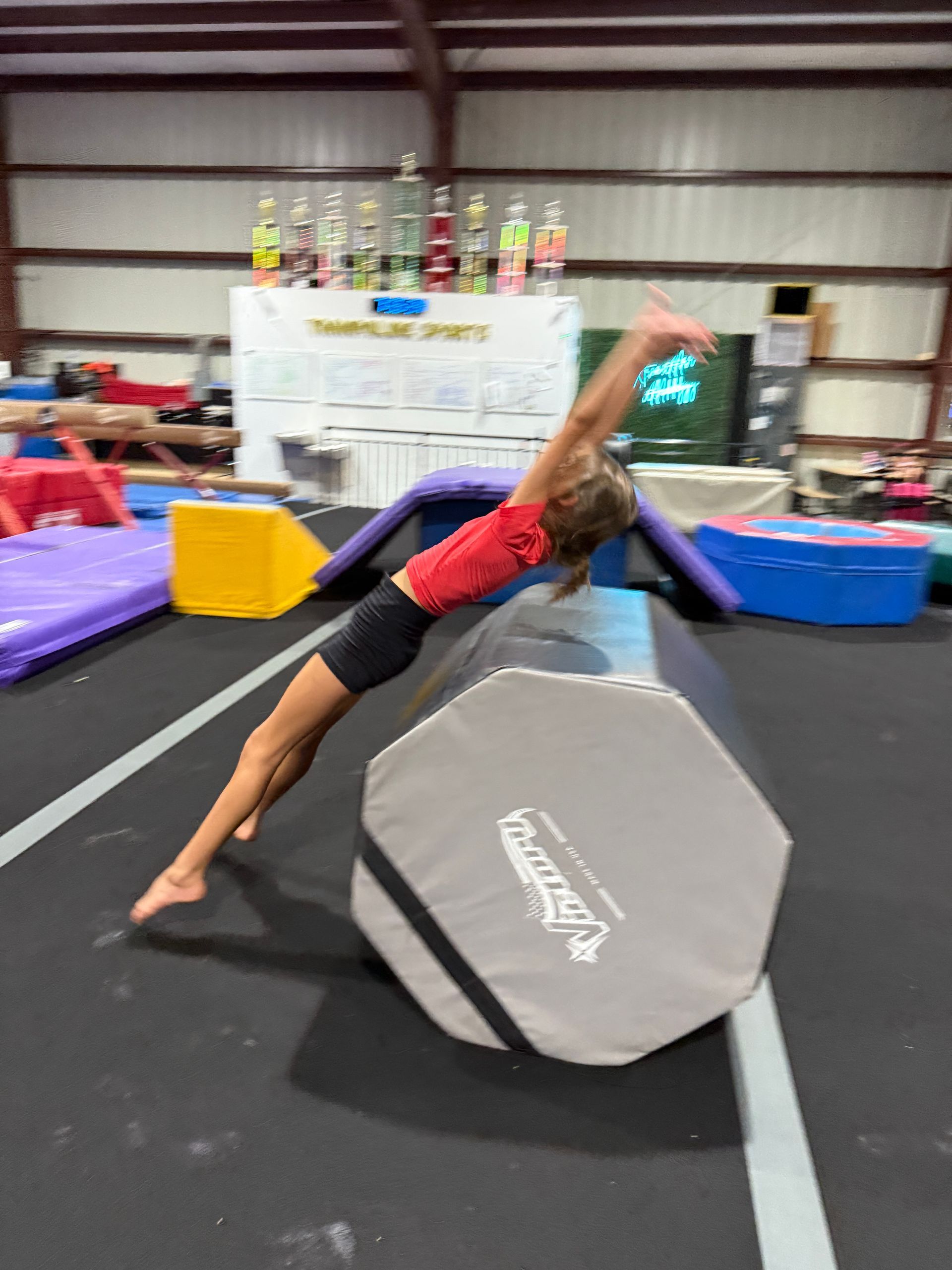 A young girl is doing a trick on a balance beam in a gym.