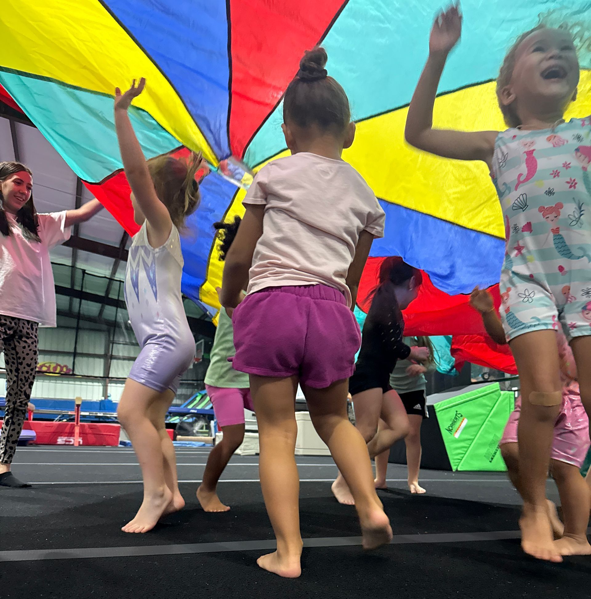 A group of young girls are dancing under a colorful parachute
