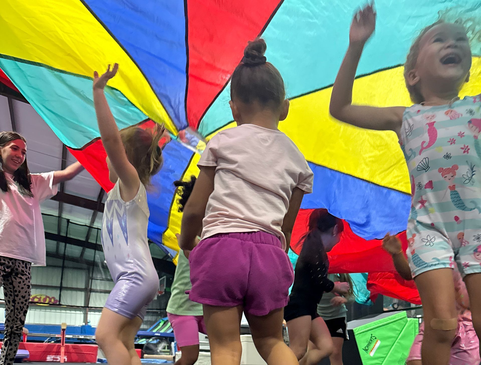 A group of young girls are dancing under a colorful parachute.