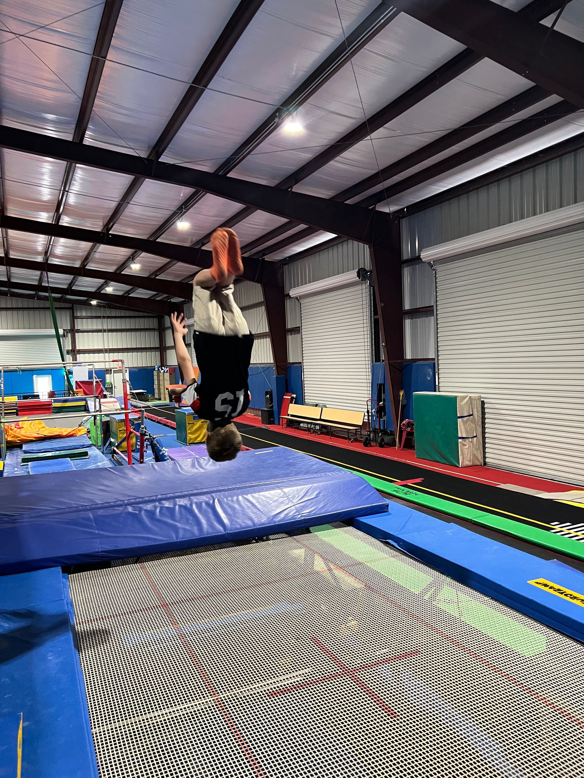 A person is doing a handstand on a trampoline in a gym.