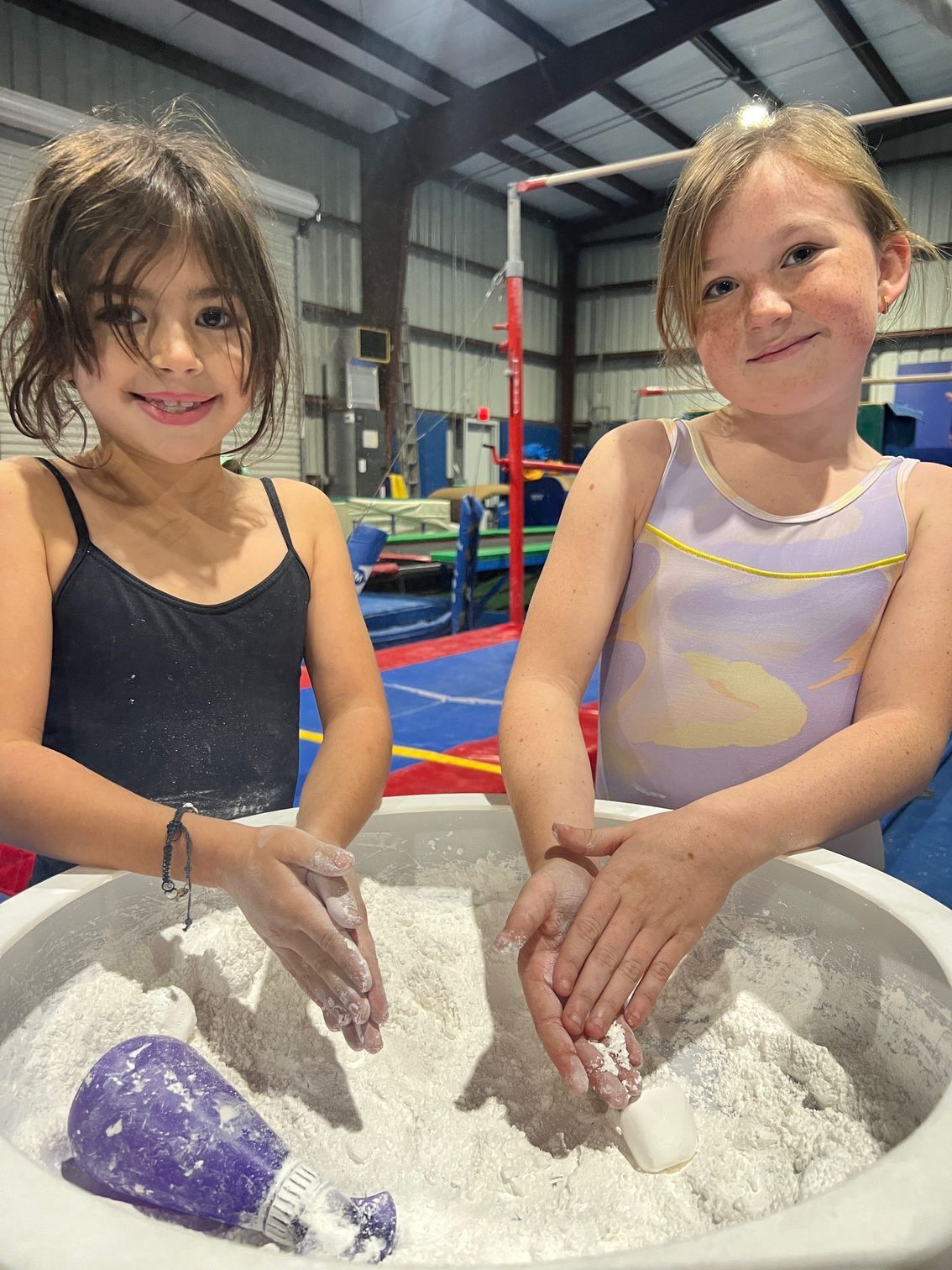 Two little girls are playing with sand in a gym.