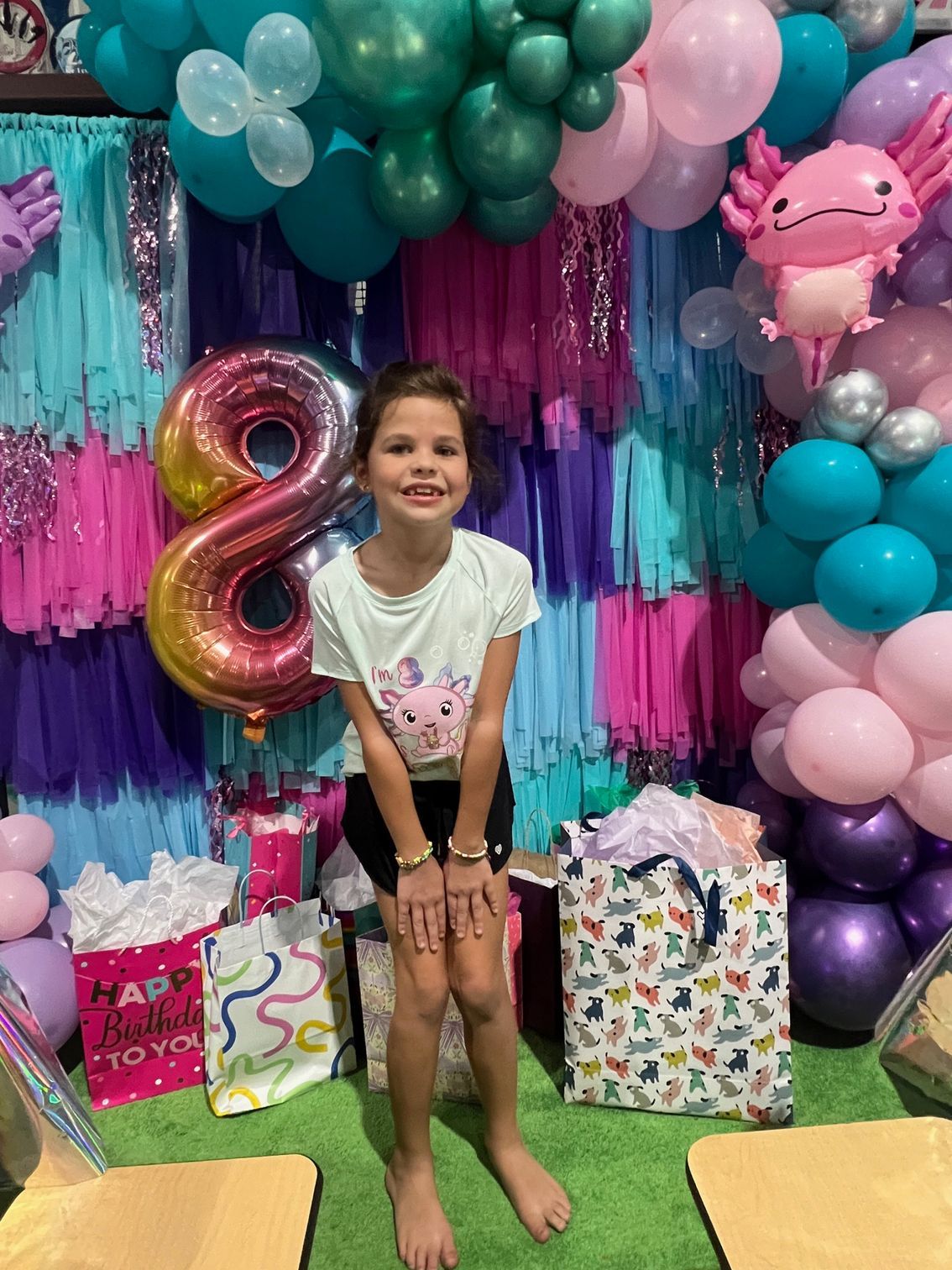A little girl is standing in front of a wall of balloons at a birthday party.