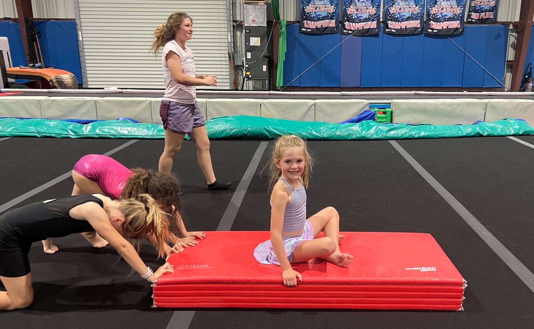A group of young girls are doing exercises on a mat in a gym.