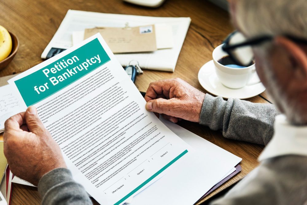 A man is sitting at a table holding a petition for bankruptcy.