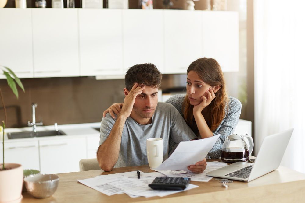 A man and a woman are sitting at a table looking at papers and a laptop.