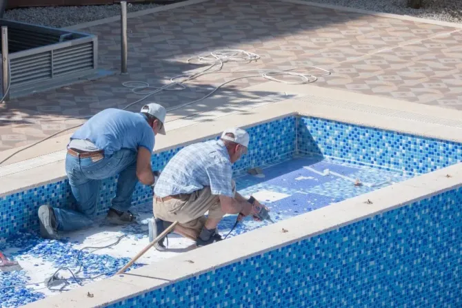 Technicians repairing tiles inside an empty commercial pool.