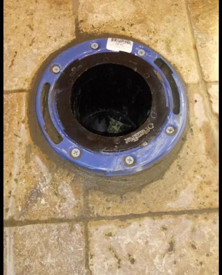 A toilet flange is sitting on a tiled floor.