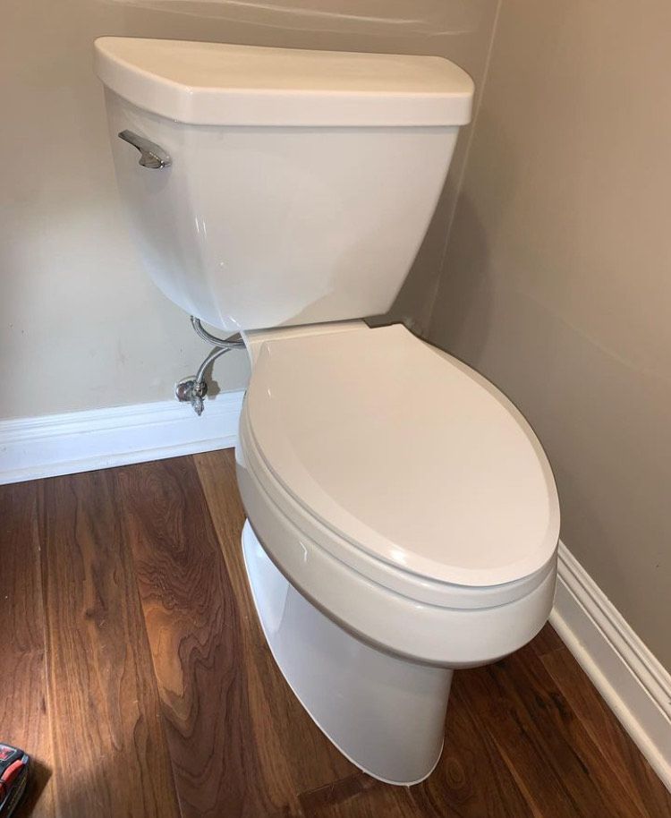 A white toilet is sitting on a wooden floor in a bathroom.