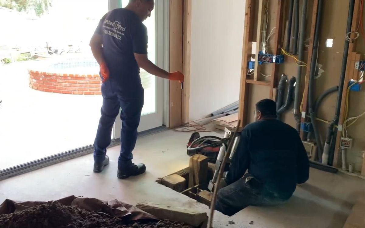 Two men are working on a hole in the floor in a room.