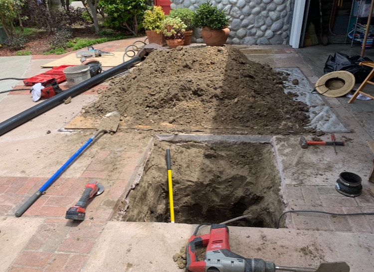 A drill is sitting on the ground next to a pile of dirt