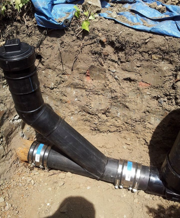 A black pipe is laying in the dirt next to a blue tarp