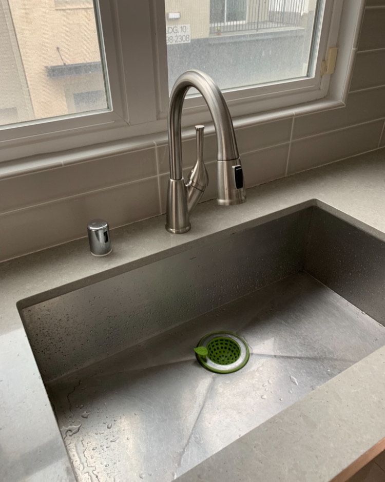 A kitchen sink with a faucet and a window in the background.