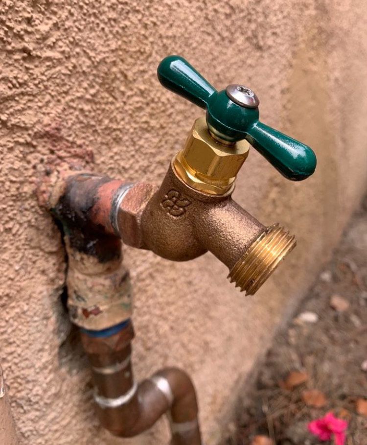 A faucet with a green handle is attached to a wall.