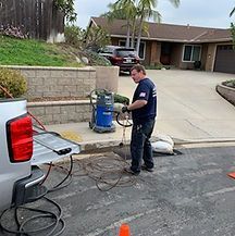 Phil Hydro Jetting Yard Drains A man is standing next to a truck in a parking lot holding a vacuum cleaner.