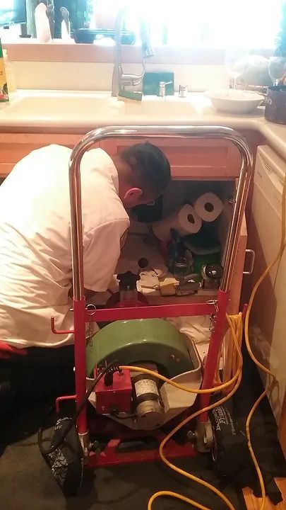 A man is working under a sink with a machine.