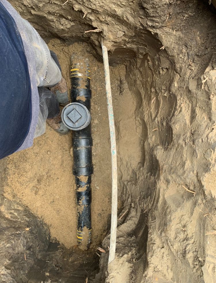 A person is working on a pipe in the dirt.