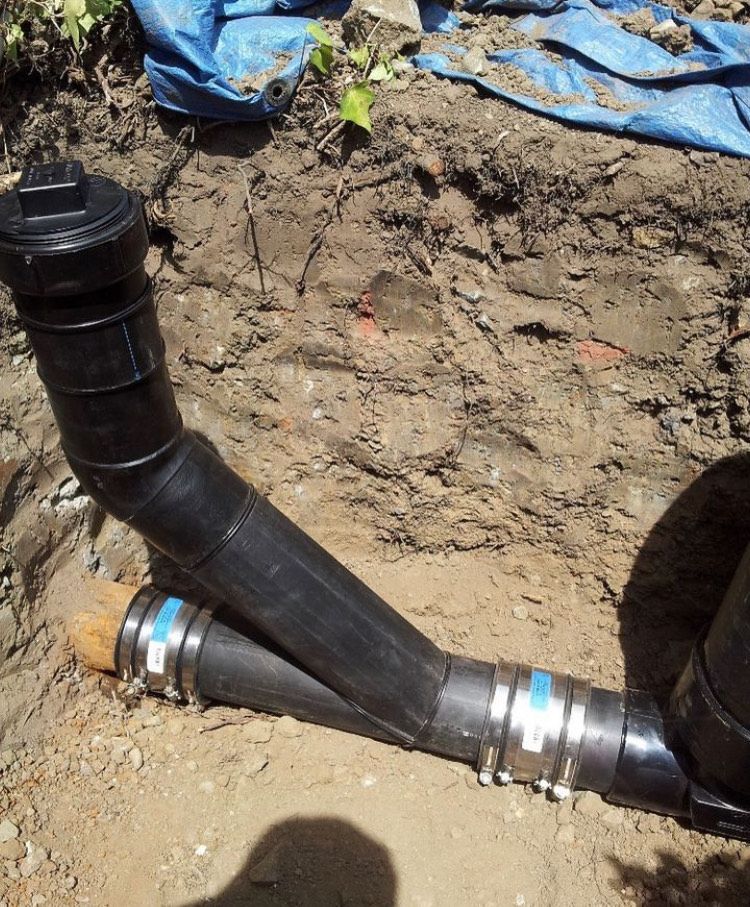 A black pipe is laying in the dirt next to a blue tarp