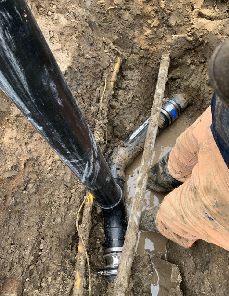 A person is working on a pipe in the dirt.