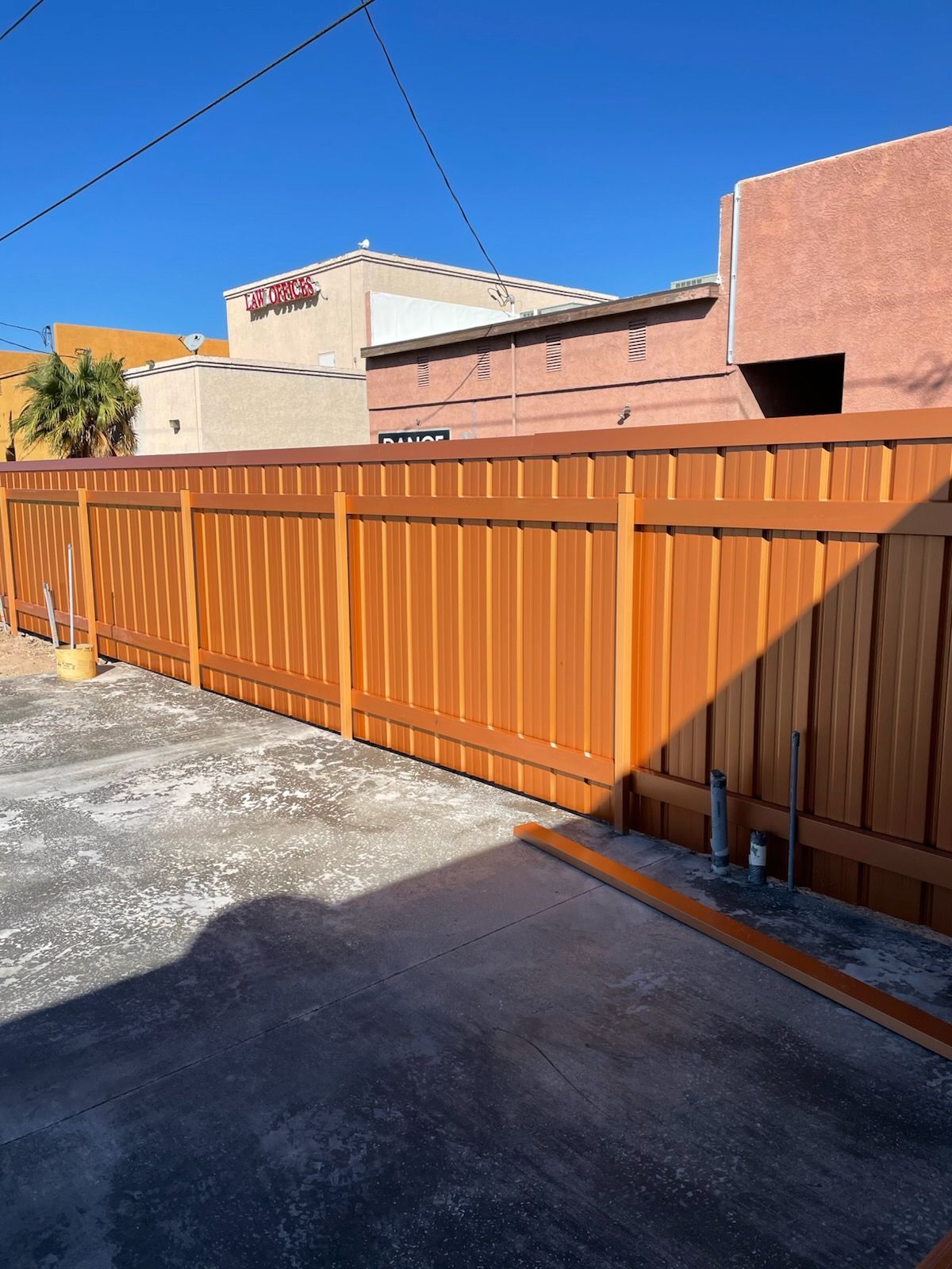 A newly stained, reddish-brown wooden privacy fence stands against a bright blue sky, with a concrete area in front.