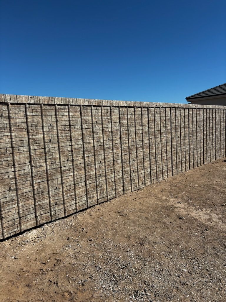 A long stone-textured perimeter wall under a clear blue sky, featuring dark vertical metal supports along its length.