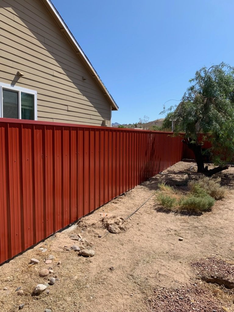Black wrought iron fence along a sidewalk, near a building with glass windows, trees, and autumn foliage.