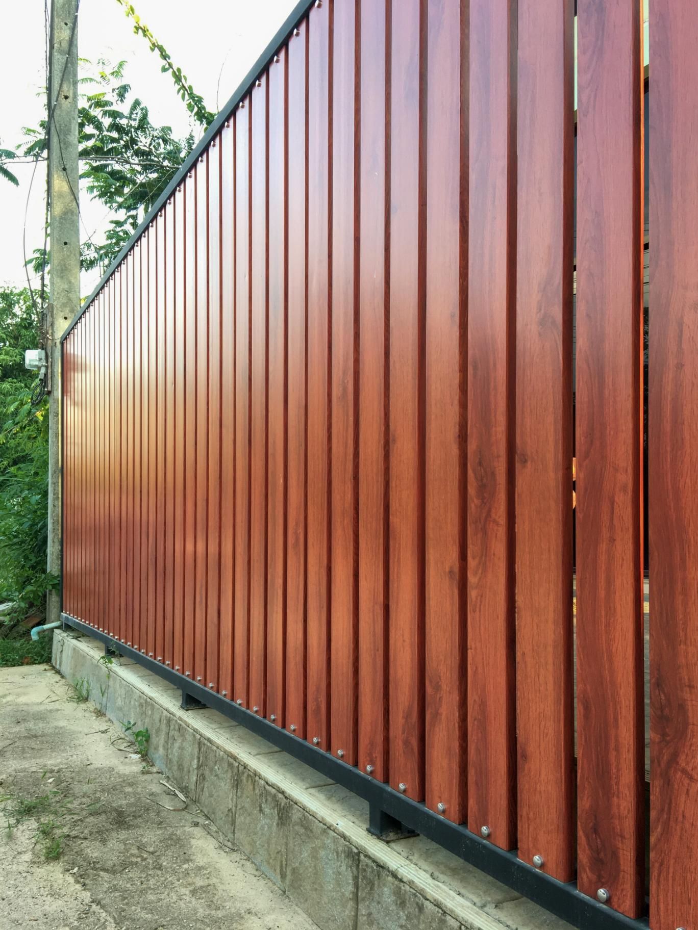 Brown vertical wooden fence with black metal frame, next to a concrete curb.