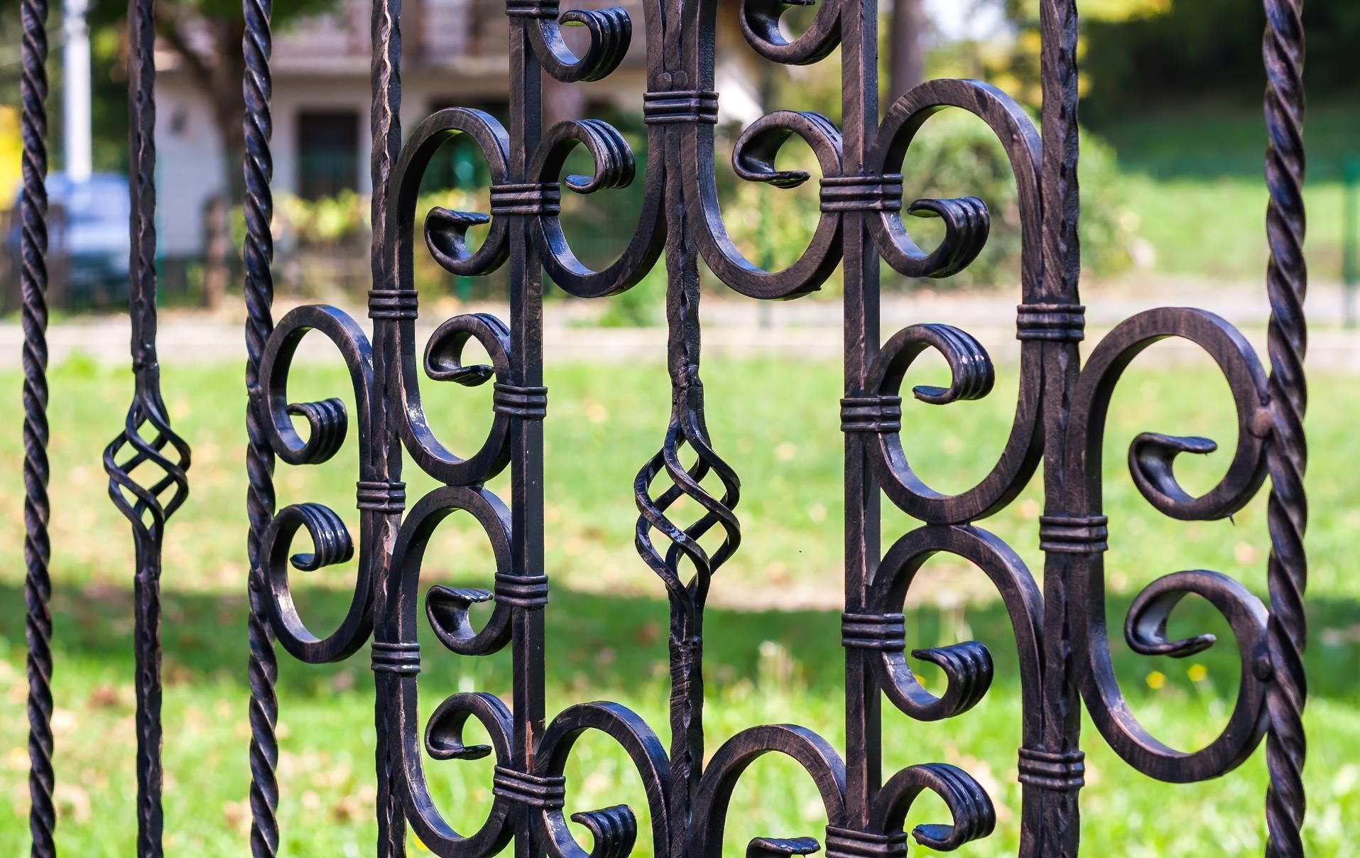 Black wrought-iron fence with decorative swirls and diamond patterns, set in a grassy yard.
