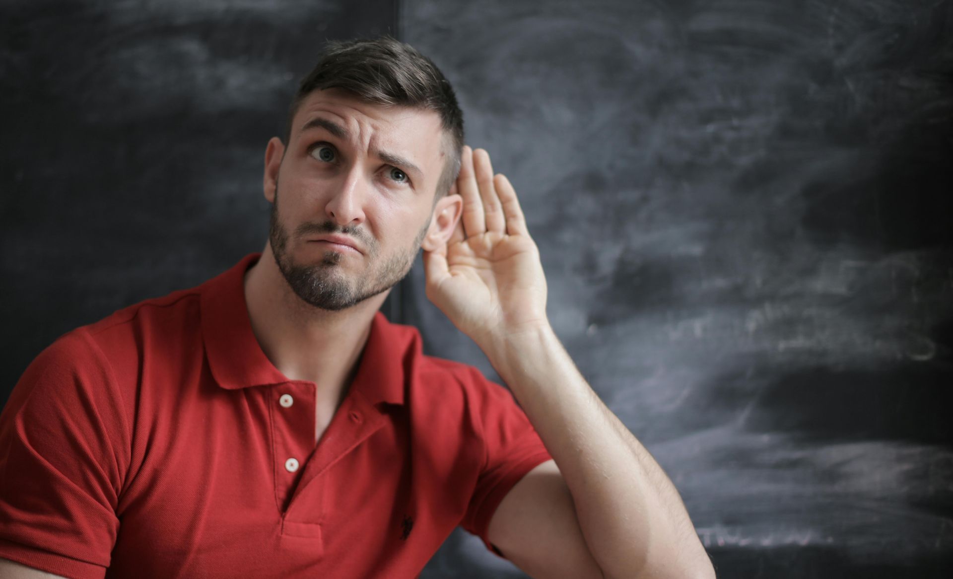 A man in a red shirt is covering his ear with his hand.