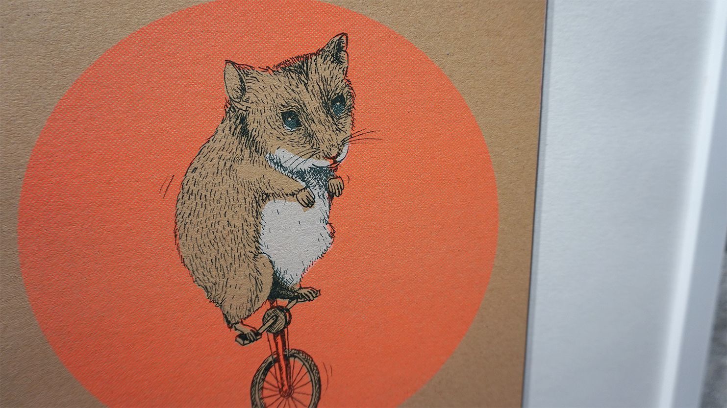 Bildauschnitt zeigt eine Illustration von einer Hamster, das Einrad fährt, mit einem orangenen Kreis im Hintergrund. Gedruckt auf braunem Umweltpapier.