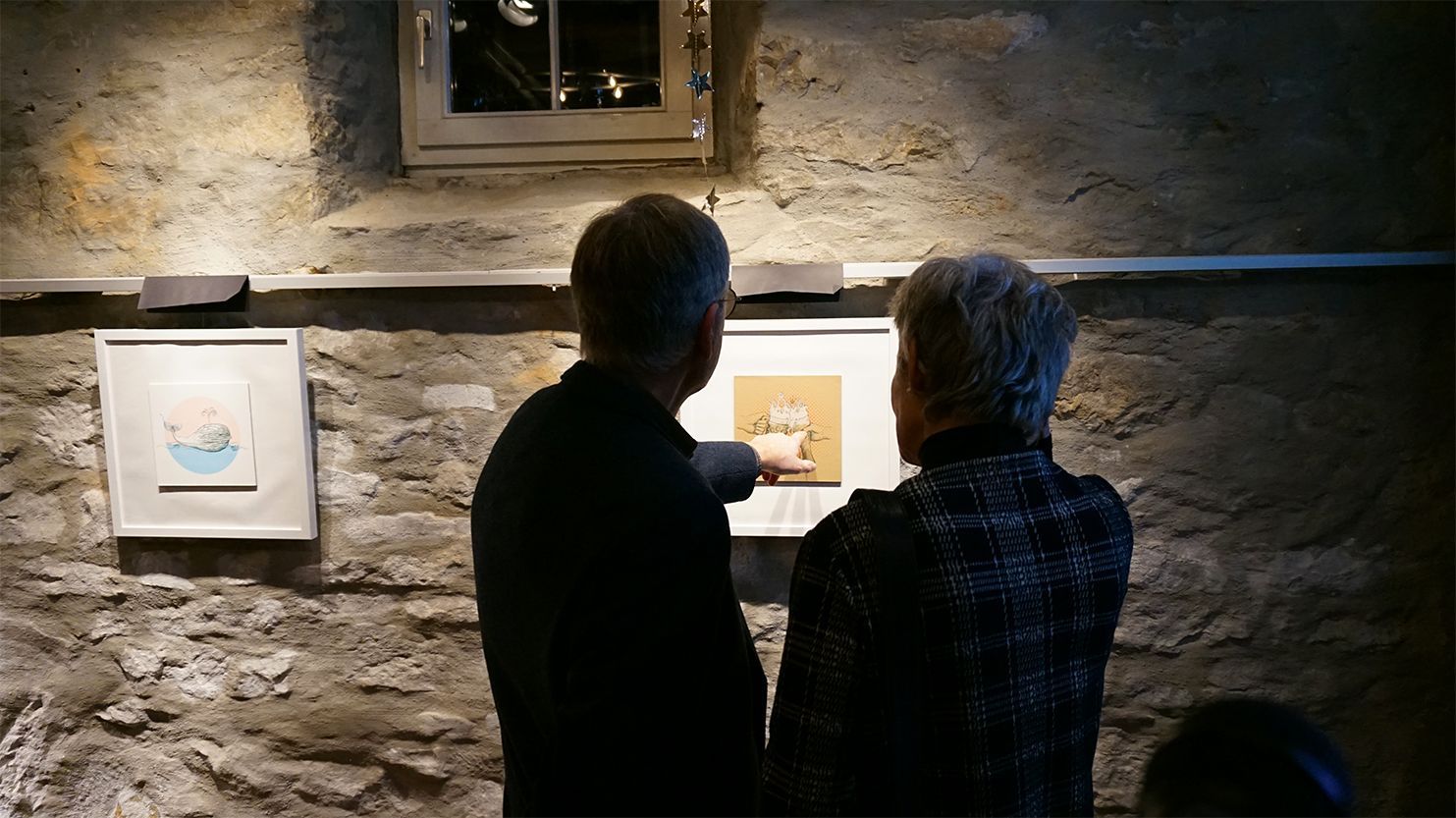 Auf dem Foto sind eine Frau und ein Mann von hinten zu sehen, die bei der Ausstellung ein Bild betrachten, auf der zwei Biergläser mit Schaumkronen abgebildet sind..