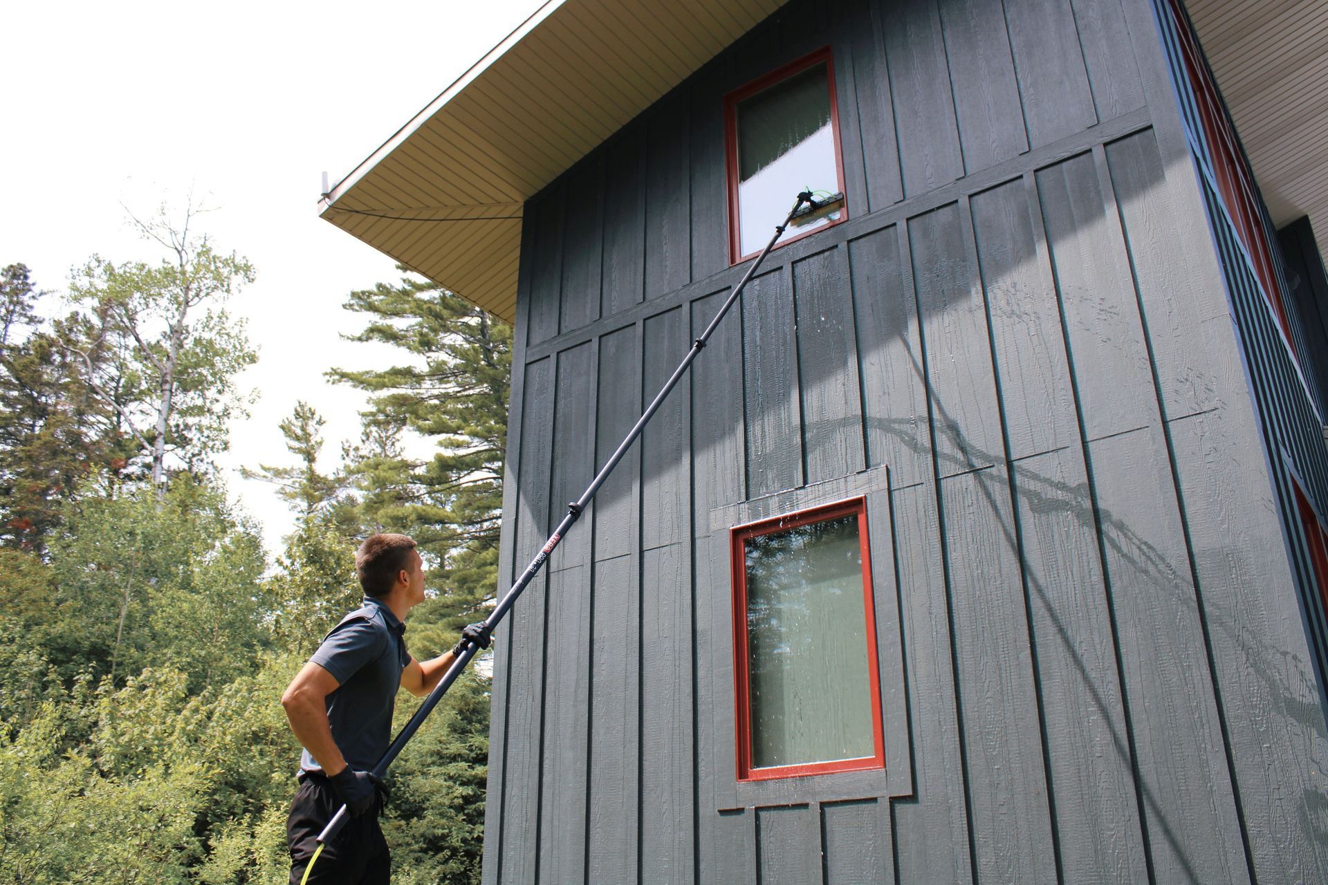 Person using a long pole to clean a second-story window on a gray house