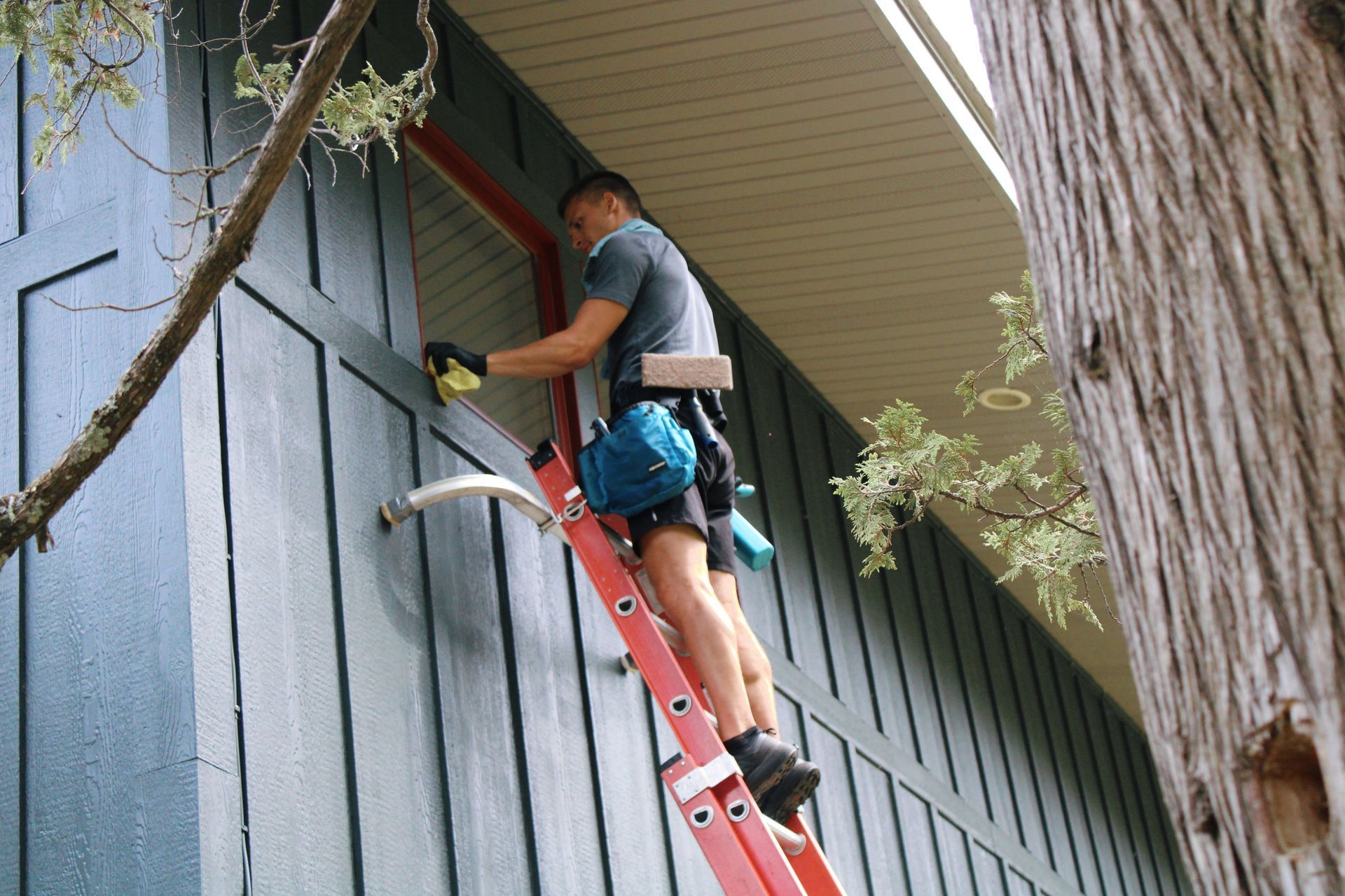Technician on a red ladder working on an exterior wall under the roof eaves