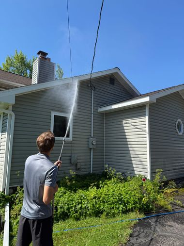 Person pressure-washing the side of a house on a sunny day