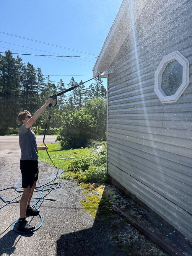Person using a hose to spray water at the side of a house on a sunny day