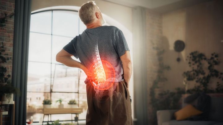 A man is standing in a living room holding his back in pain