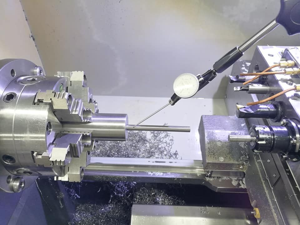 Metal lathe machining a cylindrical part with a dial indicator in a workshop.