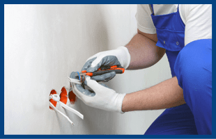 man in blue overalls wearing white gloves working on wires coming through holes in a wall