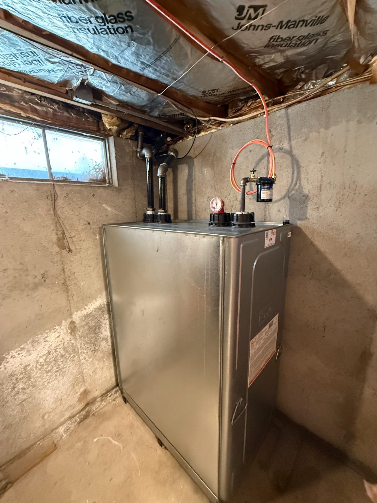 Metal furnace in a concrete basement. Black pipes, copper tubing, and gauges are visible.