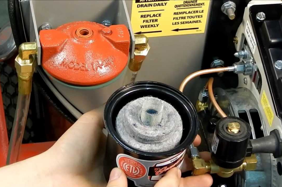 Person holding a black filter, replacing it next to an orange fuel filter housing on machinery.