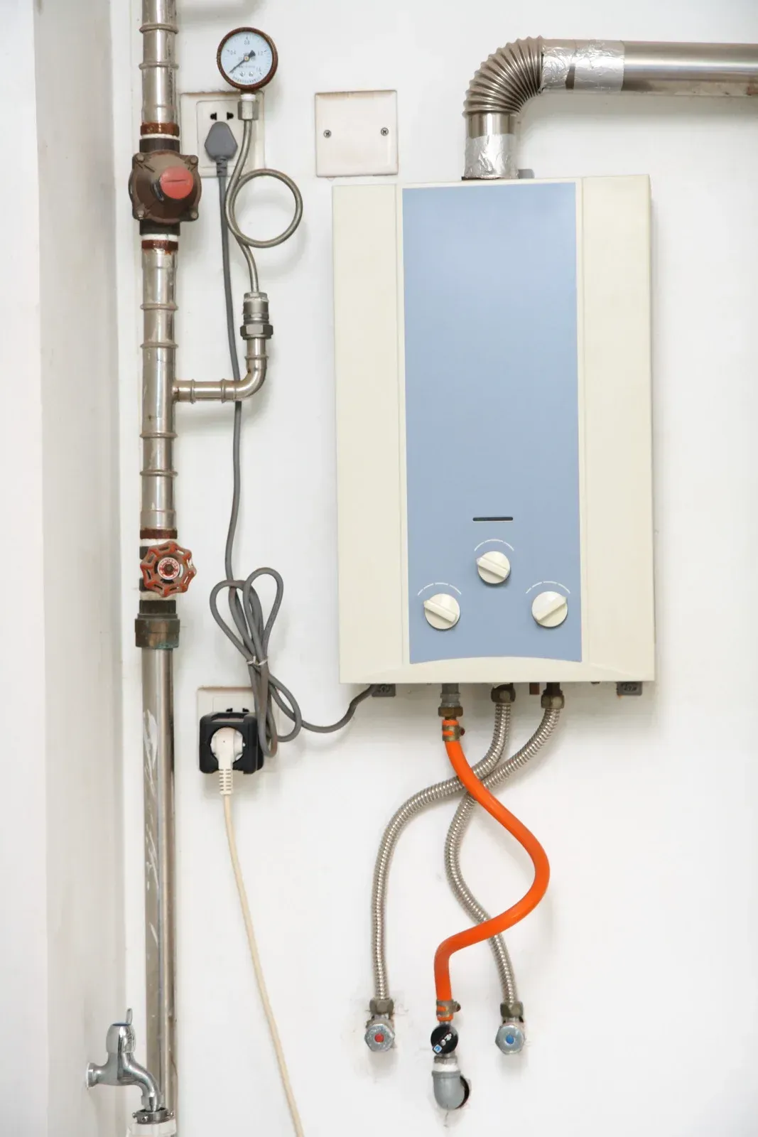 Water heater mounted on a white wall with connected pipes and electrical wiring.
