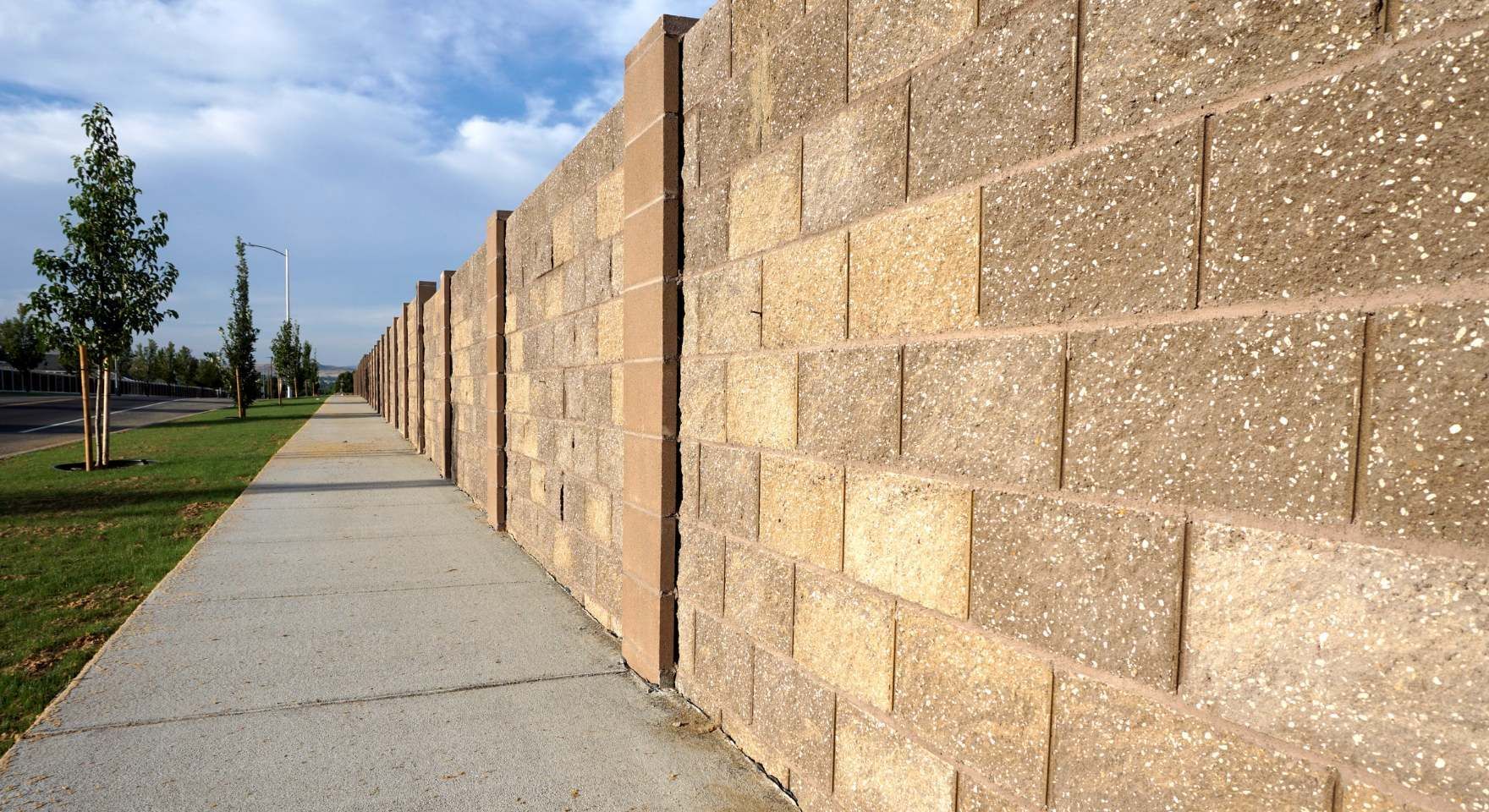 “Tall tan block wall running beside a sidewalk and grass strip during block and retaining wall services in Costa Mesa, CA”